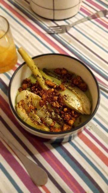 Photo d'une assiette creuse à fond plat remplie de sauce verte, de deux quarts de fenouil rôtis et de crumble de tofu doré.