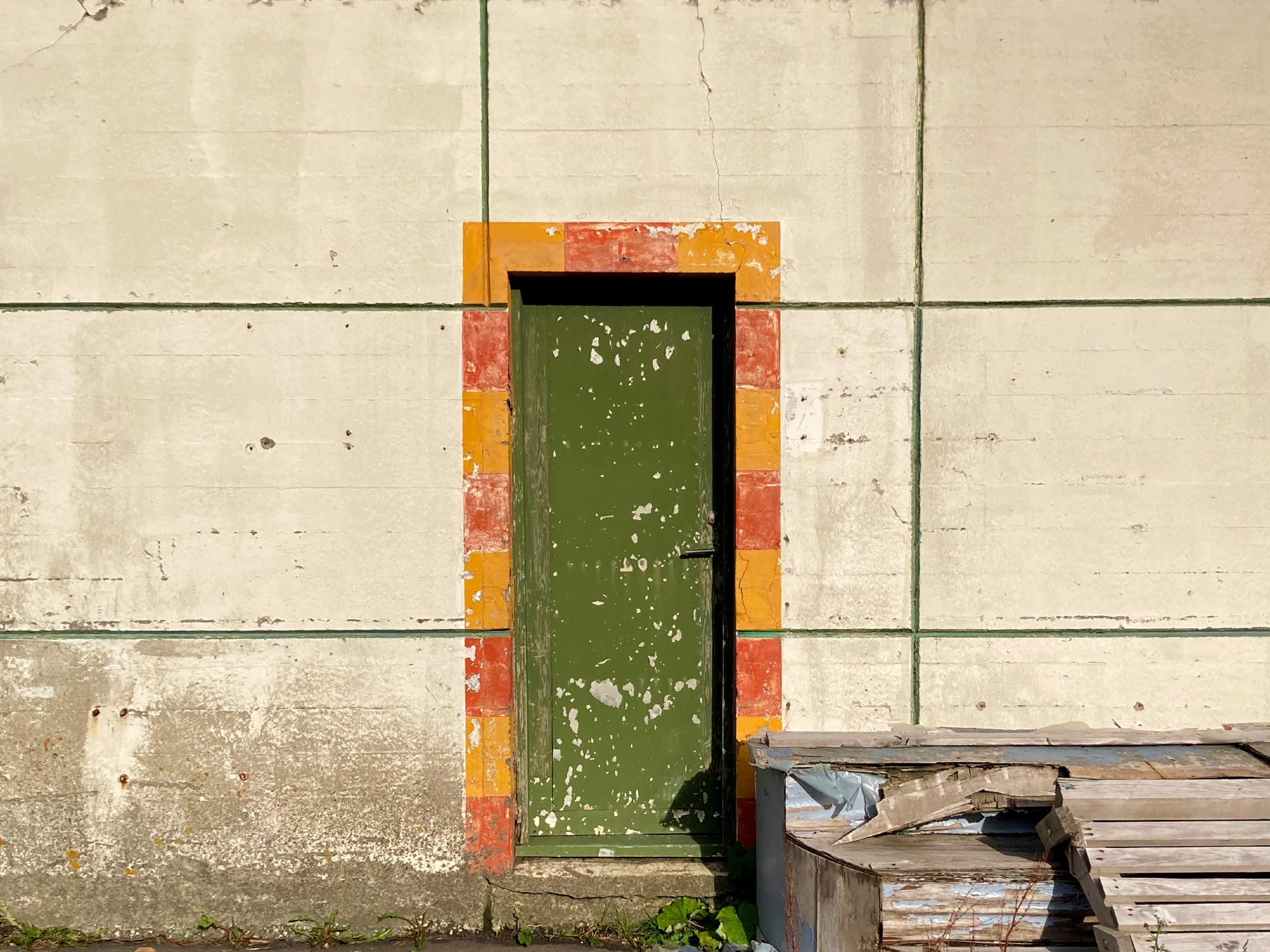 A green door with cracked paint surrounded by red and yellow stripes.