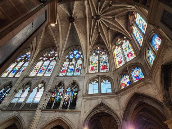 looking up at two rows of large stained glass windows just above the choir. the walls and ribbed, vaulted ceiling show the curvature of the building.