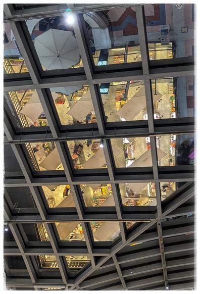 Roof of a building, metal beams form a square pattern, the space in between reflects the floor.