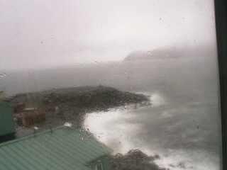 A low resolution image captured by a webcam overseeing a small peninsula with a few buildings at the front of the view.