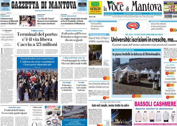Schermata di un dispositivo che mostra due prime pagine di quotidiani locali, “Gazzetta di Mantova” e “La Voce di Mantova”. L’immagine è molto scura, si vede solo lo schermo luminoso al centro circondato da buio. Sullo schermo si distinguono gli articoli principali dei giornali, tra cui titoli che parlano di terminal del porto, università, e notizie locali di Mantova. Sono presenti alcune immagini degli articoli e spazi pubblicitari, uno dei quali pubblicizza un negozio di cashmere.