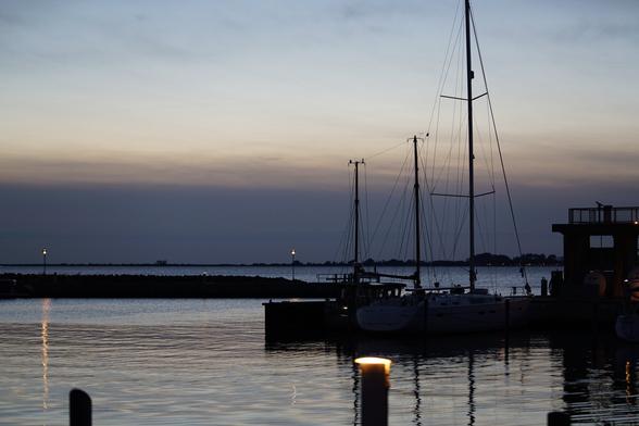 Kleiner Hafen am Abend, man sieht nur 1-2 kleine Segelboote im ruhigen Wasser des Bodden 

Lampen und deren Spiegelung, letzte Reste des Sonnenuntergangs