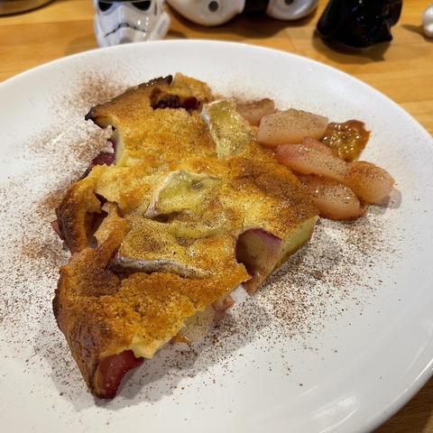 Na białym talerzu leży kawałek pieczonego naleśnika Dutch baby z plasterkami gruszki i śliwki, zapieczony z serem camembert i oprószony cynamonem. Obok znajdują się kawałki duszonej gruszki. W tle widać figurki z motywem Star Wars.