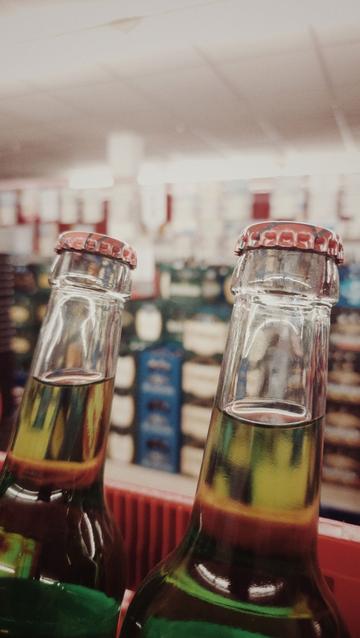 Two bottles of green lemonade in front. Boxes containing other beverages in the back, blurred, in a store.