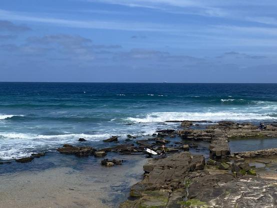 The ocean around the rocks at the southern end of Merewether Beach: such intense shades of blue and blue-green. A surfer and friend are walking towards the right over the rocks. Not sure if leaving after a good surf or repositioning to a different spot off the rocks.