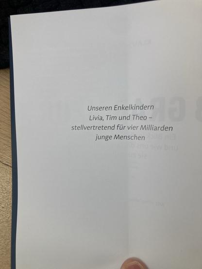 Eine offene Seite eines Buches mit einer Widmung in deutscher Sprache. Der Text erwähnt Enkelkinder namens Livia, Tim und Theo, die für vier Milliarden junge Menschen stehen.