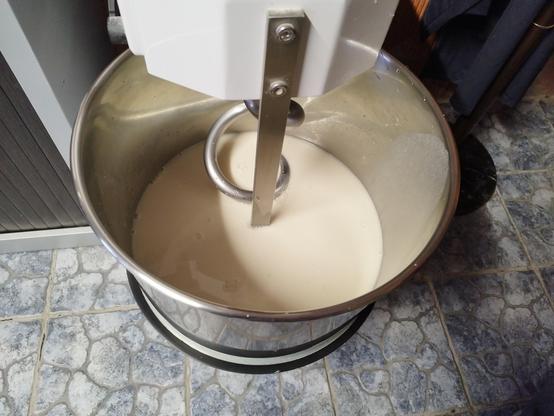 Foto de una amasadora de pan de 20Kg de capacidad. Se puede ver la cubeta de metal y el brazo en forma de espiral. Dentro hay un líquidl de color crema.