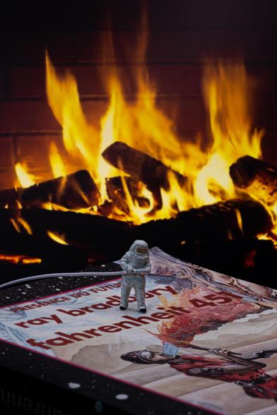 Photo of a miniature firefighter in a fireproof suit on the cover of the book Farenheit 451 by Ray Bradbury, with a fire in the background