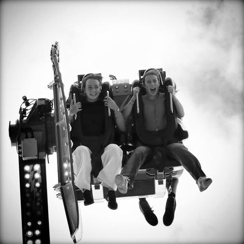 Deux jeunes femmes sont assises dans une nacelle à trente mètres de haut, dans un manège à  sensations de fête foraine 
Photo faite en contre plongée, elles regardent l’objectif et crient en souriant 
Photo prise avec leur consentement