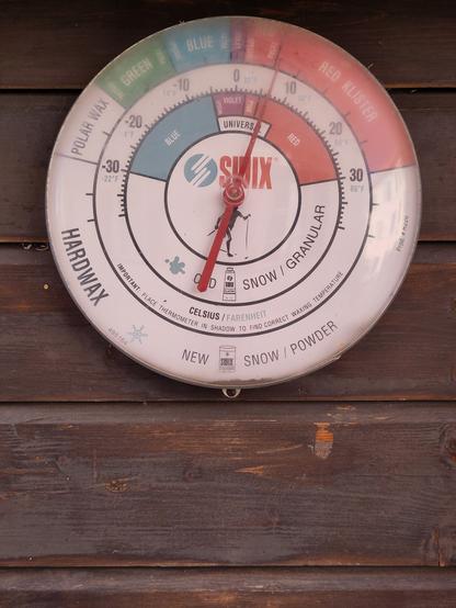 Foto. Kreisrunder Thermometer, die Skala ist mit Produktenamen für Langlaufwachs ergänzt.