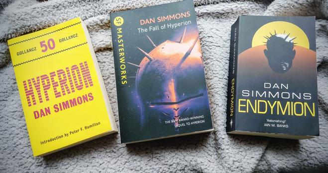 Three paperback books laid out on a grey fleece throw. 

They are Hyperion, The Fall of Hyperion and Endymion by Dan Simmons, all part of the series called the Hyperion Cantos. None of the editions have matching covers.