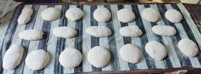 Foto de una mesa rectángular de unos dos metros de largo. Tiene una tela de rayas gruesas, blancas y negras. Encima hay diecinueve piezas de masa sin cocer.