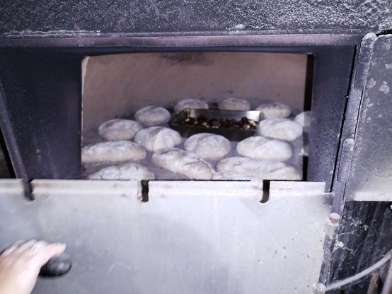 Foto de un horno de pan, tiene la puerta dividida en dos, la puerta de abajo está cerrada y a través del hueco que queda ae ven unas piezas de pan y un recipiente metálico con castañas dentro.