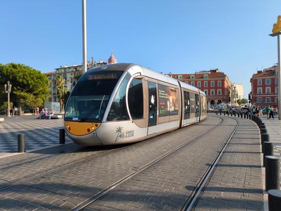 Moderne Straßenbahn, die gerade um die Ecke fährt. Blauer Himmel, im Hintergrund Häuser.