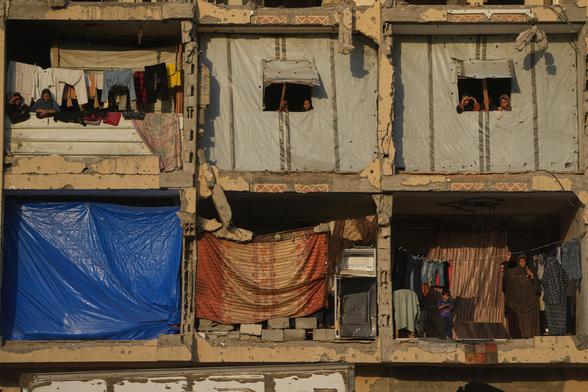 Desde un edificio dañado convertido en refugio, mujeres palestinas observan a miembros del grupo militante Hamás buscando los cuerpos de los rehenes en una zona de la Jan Yunis, en el sur de la Franja, el 17 de octubre.