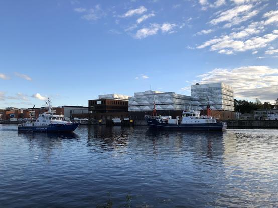 Vor dem Geomar-Gebäude begegnen sich zwei blaue Schiffe, Polizei und ein Forschungsschiff. Blau der Himmel und das Wasser.