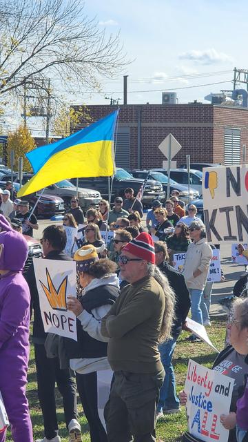 A large group of people are gathered outdoors, likely at a protest or rally, with signs and a Ukrainian flag prominently displayed. Several individuals are holding signs with various messages, some of which are partially visible. The foreground features a person with a sign that reads “NOPE” in large yellow letters. A person in a red hat and jacket is facing the camera. In the background, a Ukrainian flag waves, and other signs with text are visible, including one that reads “Liberty and Justice for ALL”.

Provided by @altbot, generated privately and locally using Gemma3:27b