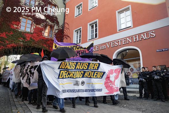 Die Demonstrationsspitze am Oberer Markt, zu sehen sind mehrere Banner. Auf einem ist "Nazis aus der Deckung holen!" zu lesen, es handelt sich um das Frontbanner. Darüber hinaus schützen sich die Demonstrant*innen mit aufgespannten Regenschirme vor der filmenden Polizei und den zahlreichen rechten Medienaktivisten.