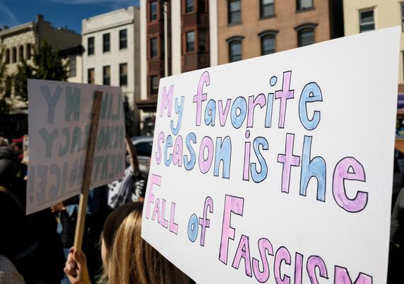 In a crowd of people holding protest signs, we see one which reads: "My favorite season is the Fall of Fascism"