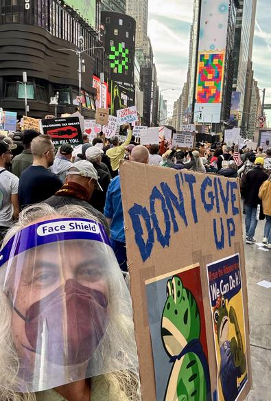 Selfie of me in mask & face shield, with sign. View is Times Square marchers, South.