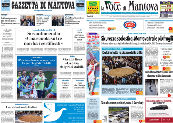 Prima pagina di giornali locali proiettata su uno schermo.  Nell’immagine si vedono due prime pagine di quotidiani: “Gazzetta di Mantova” e “La Voce di Mantova”. Sono affiancate e mostrano articoli di attualità locale. Alcuni titoli visibili:  Per la Gazzetta di Mantova: - Titolo principale: “Sos antincendio: ‘Una scuola su tre non ha i certificati’” - Sotto, una foto di una squadra sportiva con la didascalia: “Il Mantova decima, ma non basta: ‘La partita giùda verticella’” - Altri titoli minori: “Via alla fiera: la casa dei pirati stabili” e “Una sbracciolata da Festival”  Per La Voce di Mantova: - Titolo principale: “Sicurezza scolastica, Mantova tra le più fragili” - Sotto, una foto di una folla e il titolo: “Dolci in tutte le piazze della città” - Alcuni titoli minori: “Non ci sono espositori, salta il CarpiAuto” e “Noleggio a breve termine: molto bene”