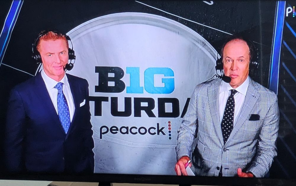 two sportscasters standing on either side of a desk with a B1G SATURDAY on Peacock background behind them. the man on the left unfortunately blocks the letters SA and the man on the right unfortunately blocks the letters AY, leaving BIG TURD PEACOCK as the only visible text.