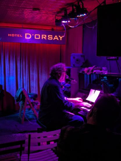 A photo of Davis Rogan singing and playing the upright piano at Barbes in Brooklyn.