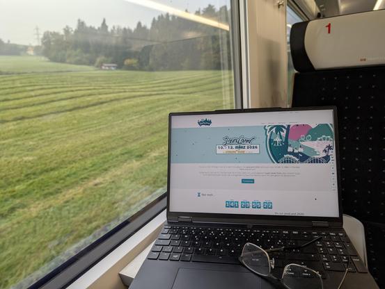 Ein Foto von einem Notebook mit der JavaLand Webseite vor dem Fenster im Zug. Draussen ist eine grΓΌne Wiese zu sehen mit einem kleinen WΓ€ldchen. Auf der Tastatur des Notebooks liegt eine Lesebrille.