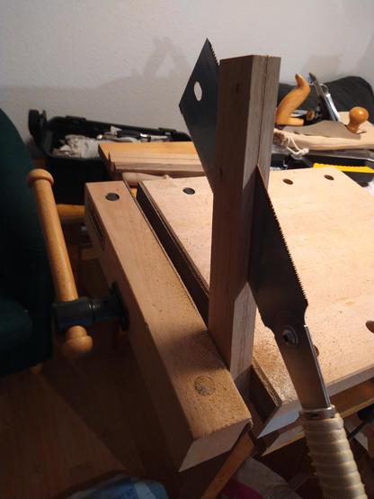 Im Schraubstock einer mobilen Werkbank ist ein Kantholz eingespannt, das mit einer Zugsäge längs aufgetrennt wird. Im Hintergrund weitere Holzwerkzeuge.