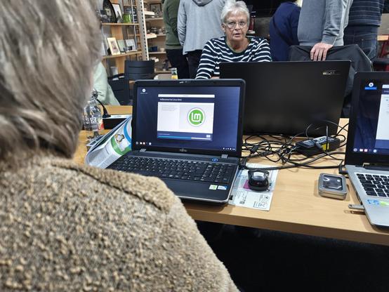 Eine Person von hinten, die vor einem Notebook sitzt. Auf dem Notebook ist das Linux Mint Logo zu sehen.