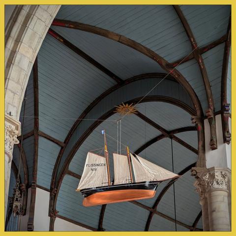 scale model of a fishing boat with sail, with the background of the blue-gray painted ceiling of a church