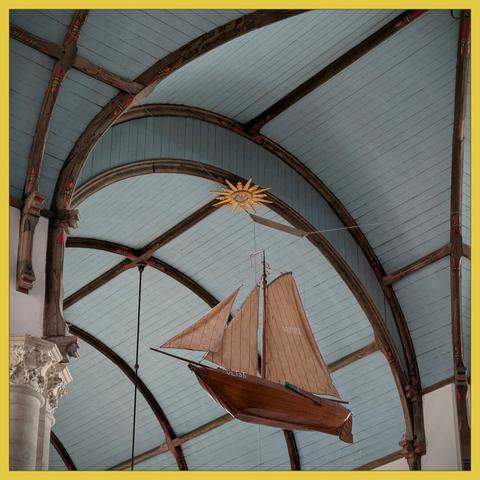 scale model of a fishing boat with sail, with the background of the blue-gray painted ceiling of a church