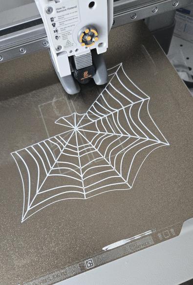 Photo of a 3D printer bed with a spider web being printed.