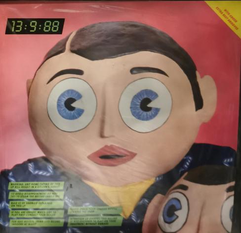 LP cover for 13:9:88 by Frank Sidebottom. Cover shows Frank and little Frank (both have paper mache heads). The cover has a number of statements in the bottom corner.