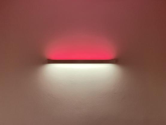 An horizontal neon light in the middle of a wall with the top glowing red while the bottom glows white.