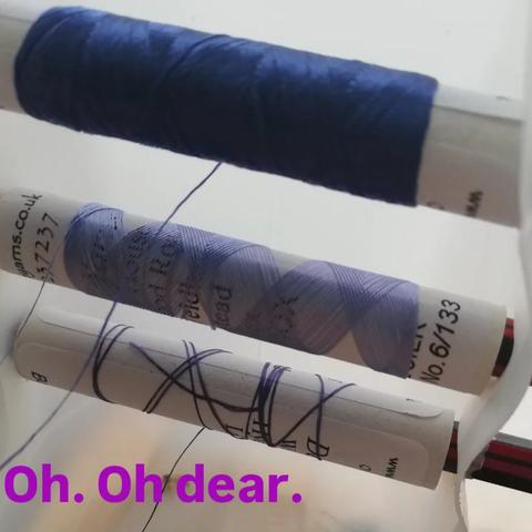 Photo of my spool holder (made out of a plastic milk bottle), with three spools on it. The top on is ok, the second is down to the last couple of layers of thread, and the second is down the last few loops.
Text in violet below the last spool reads "Oh. Oh dear."