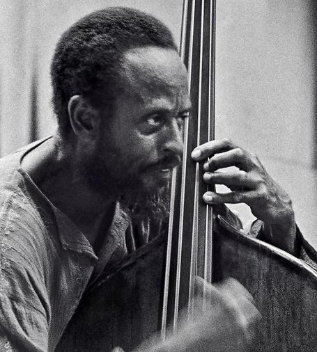 Black and white photo of a black man ((Percy Heath) holding an upright bass and looking sternly to the right side of the frame