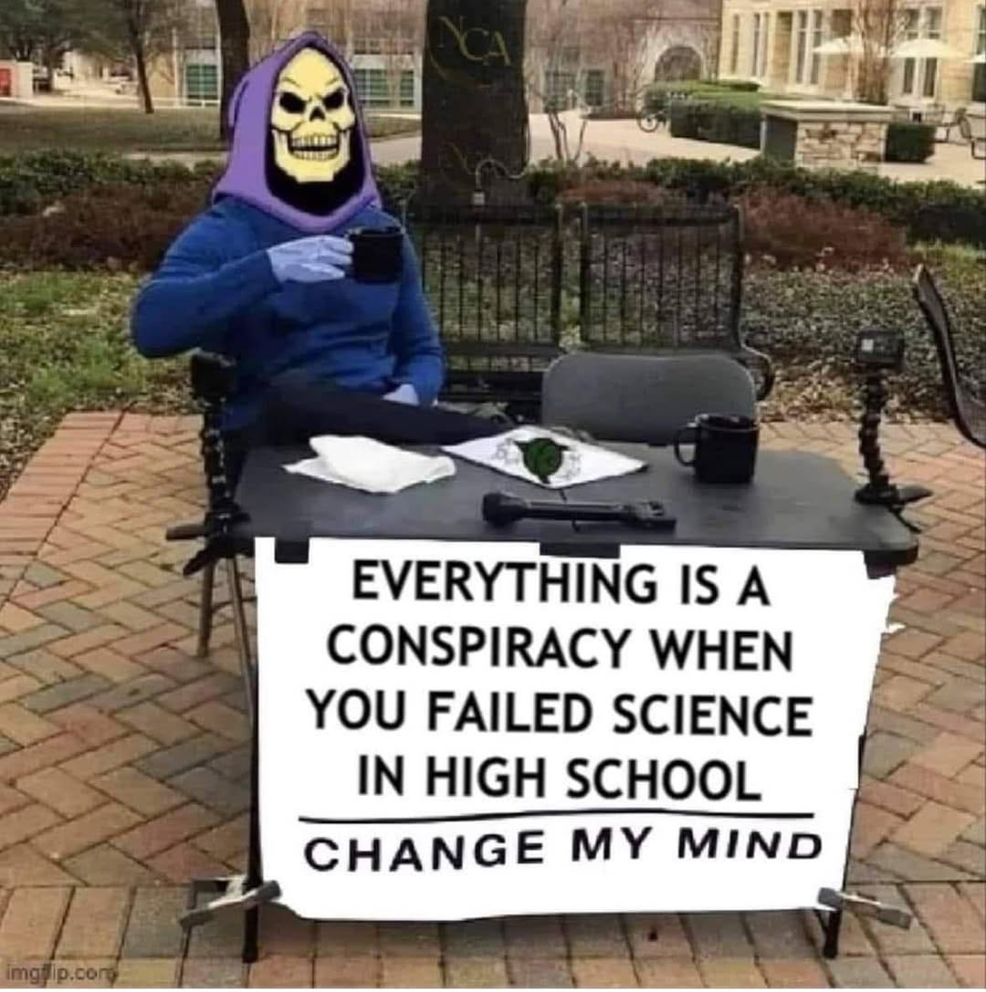 someone in a skeleton costume sitting at a table with a sign saying: "EVERYTHING IS A CONSPIRACY WHEN YOU FAILED SCIENCE IN HIGH SCHOOL CHANGE MY MIND"