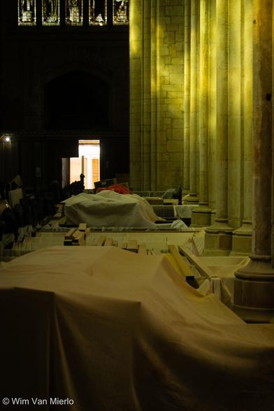 Inside the church during building work. Various objects are covered in sheets to protect them from dust.  The light is playing on the stone pillars.