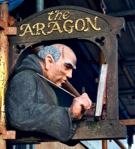 A wooden pub sign of a monk writing in a book with a quill.