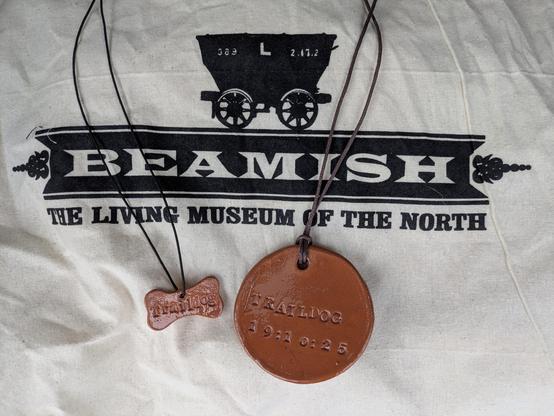 Close-up of a tote bag showing the Beamish Museum logo, with human and dog pottery medals displayed on top