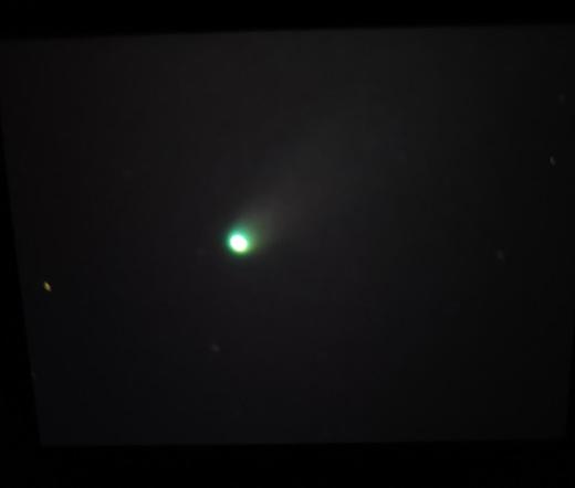 Un cometa de color verdoso en fondo negro con algunas estrellas.