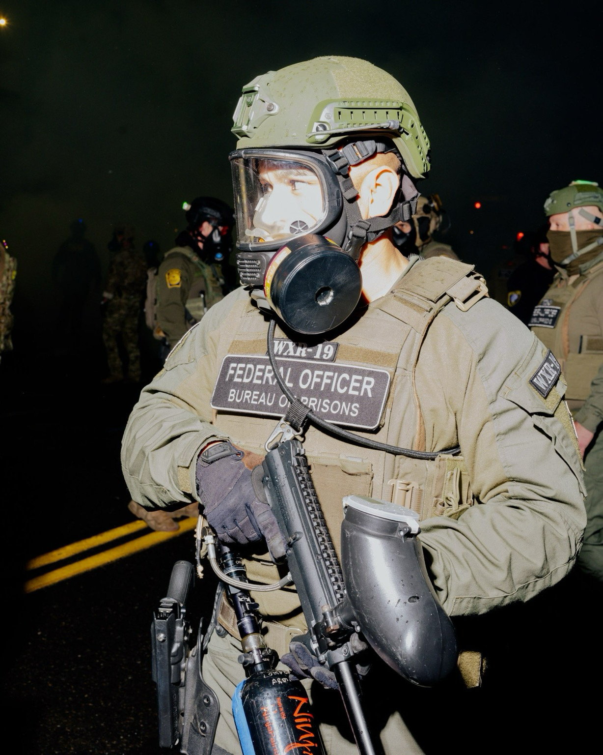 Federal agent in fatigues with a patch that says “WXR-19 federal bureau of prisons”