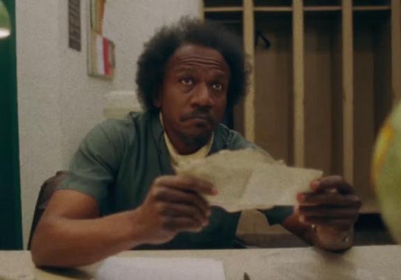 A man holds a piece of ripped paper in his hands, looking up at someone and looking pensive.