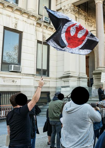 A protester holds aloft the flag of the Alliance to Restore the Republic (from Star Wars).  Protesters' faces are obscured with black discs.