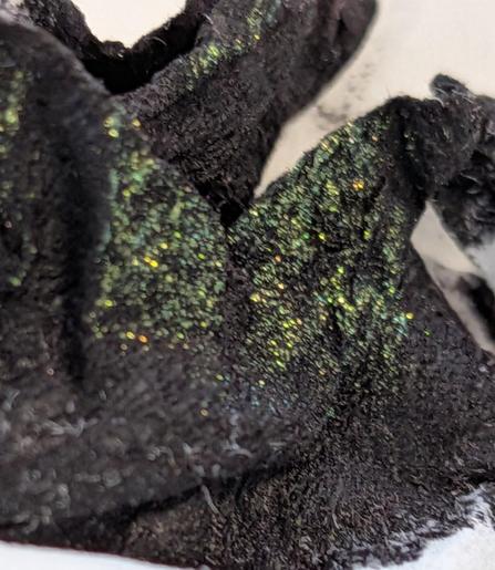 A crumpled tissue with a splodge of Astral ink, which looks black, with a shimmer of mostly gold, that can catch the light with other colours.