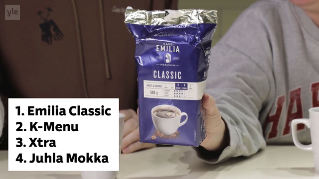 Kuvakaappaus Ylen jutun videosta. Vasemmassa alanurkassa laatikko jossa teksti:

1. Emilia Classic
2. K-Menu
3. Xtra
4. Juhla Mokka 

Muuten kuvassa harmaaseen paitaan pukeutuneen ihmisen käsi pitelee lilansinistä Emilia Classic -kahvipakettia.