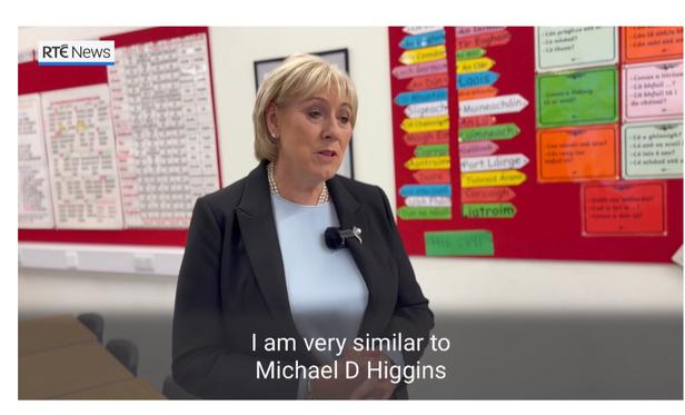 Screenshot of Heather Humphries standing in a school giving an interview. The caption as she is talking is “I am very similar to Michael D Higgins”.