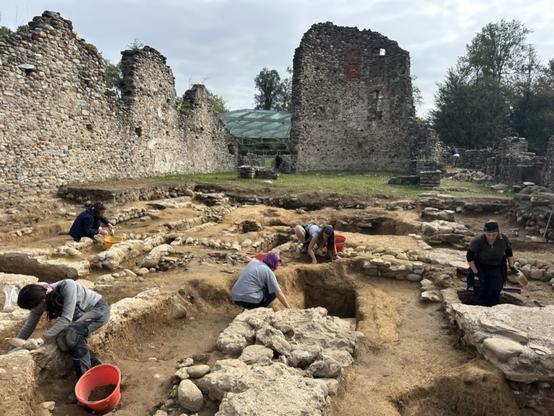 Scavi archeologici in corso al Parco Archeologico di Castelseerio, con diversi ricercatori che lavorano tra le rovine di un'antica edificazione.
